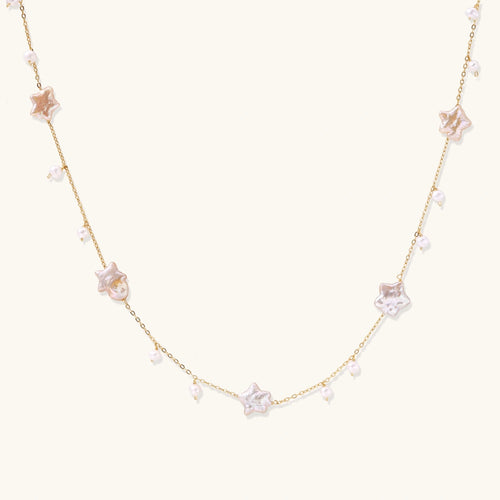 Gold plated chain with iridescent star-shaped shell pearls and small round shell pearl drops on cream background.