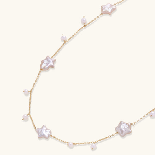 Gold plated chain with iridescent star-shaped shell pearls and small round shell pearl drops on cream background.