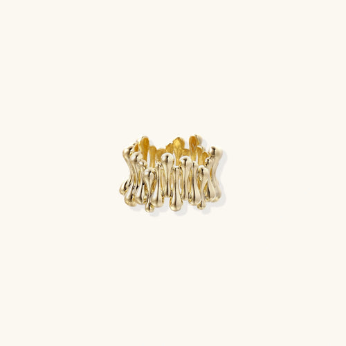 Gold-plated ring with rows of tiny gold droplets wrapping a wide sculptural band on beige background