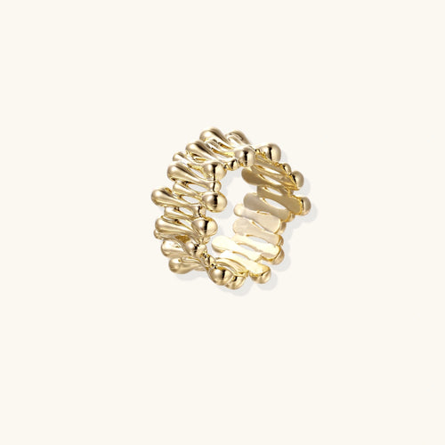 Gold-plated ring with rows of tiny gold droplets wrapping a wide sculptural band on beige background